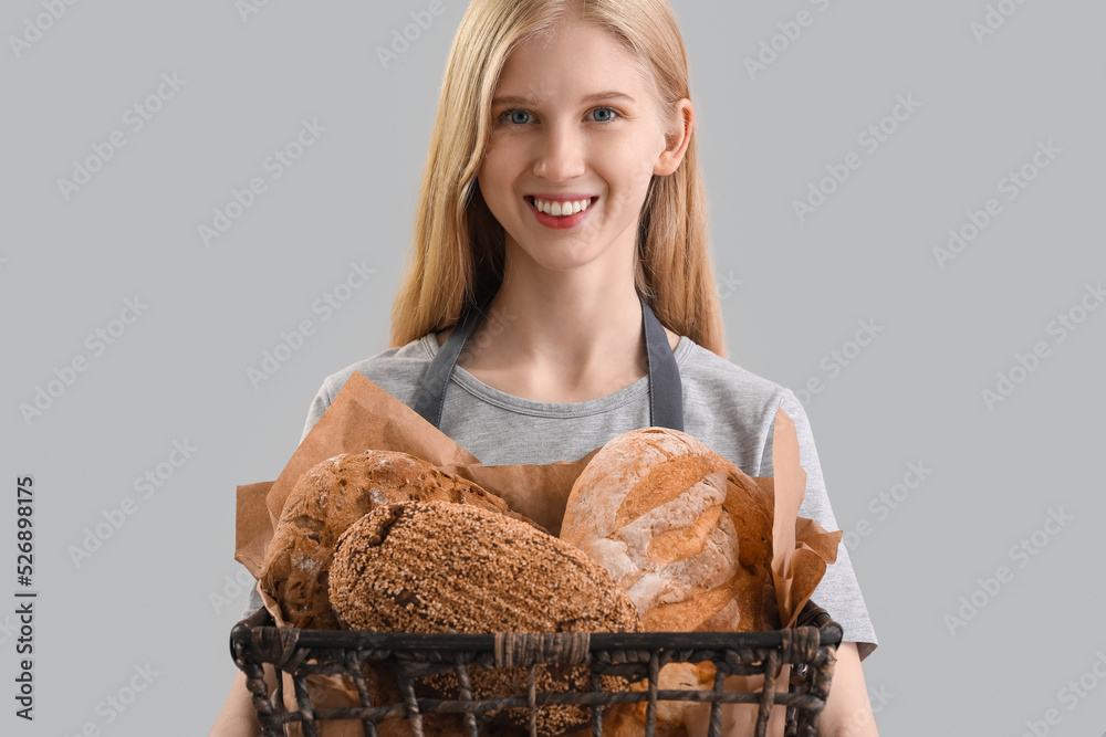 Young woman holding basket with fresh bread on grey background