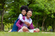 African American mother is playing piggyback riding and hugging with her young daughter while having a summer picnic in the public park for wellbeing and happiness concept
