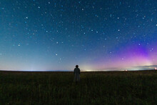 Abstract Night Photo Of A Figure Of A Lonely Person In A Field Under A Starry Sky And Northern Lights, Starfall. Astrophotography