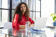 Attractive cheerful business woman in red shirt working on laptop at modern office.