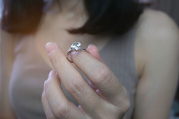 Wall Mural - Close up of woman's hand holding an elegant diamond ring with sunlight and shadow background. love and wedding concept. Soft and selective focus.