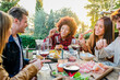 Group of multiethnic friends living healthy lifestyle and smiling and joking while doing aperitif and drinking red wine at outdoor pub restaurant