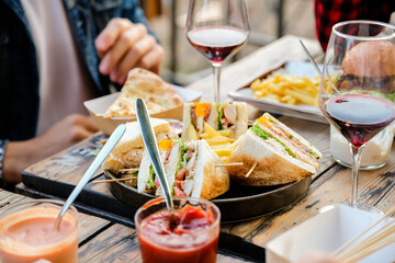 Close up of aperitif table. Friends dining together at brewery pub restaurant, with club sandwich, glasses of wine and french fries