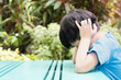 Close up of Asian autistic student child sit at table at school cover ears with hand and close eyes due to stress and anxiety. Autism stimming behavior for World Autism spectrum awareness day concept