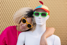 Smiling Woman With Mannequin Wearing Sunglasses In Front Of Wall