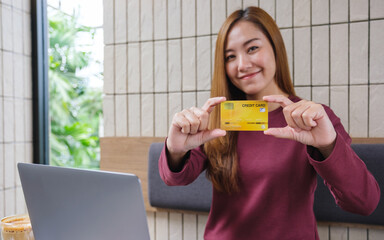 Wall Mural - Portrait image of a young woman holding and showing credit cards while using laptop computer for online payment