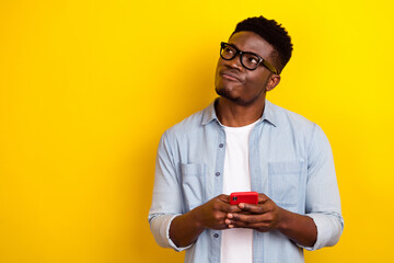 Photo of think millennial brunet guy hold telehone look promo wear eyewear jeans shirt isolated on yellow color background