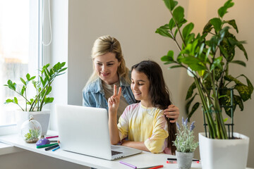 Wall Mural - Beautiful young woman and her little cute daughter are using laptop at home. Enjoying spending time together