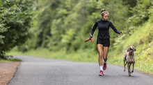 Young Female Holding Leash Releases Her Dog On An Empty Road During Jogging