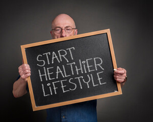 Wall Mural - start healthier lifestyle blackboard sign held by a senior man, teacher, mentor or presenter