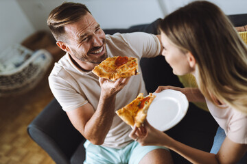 Wall Mural - Happy young couple eating pizza for lunch in the living room