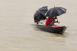 Men in a wooden canoe sheltering under umbrellas from the monsoon rain, Bangladesh