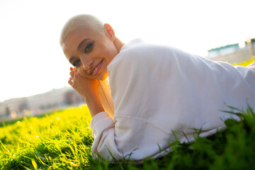 Wall Mural - Portrait of young smiling millenial european short haired woman lying on green grass meadow summer park. Beautiful happy blonde girl outdoor.