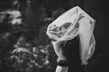 Romantic wedding moment, bride and groom smiles to each other under the veil, happy and joyful moment on nature in the park. Black and white photo.