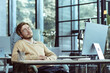 Tired IT specialist engineer programmer sleeps in the office at the table during the day, man in glasses and casual clothes works at the computer, businessman rests