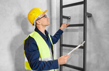 Architecture, Construction And Building Concept - Male Builder Or Worker In Helmet And Safety West With Clipboard Climbing Ladder Or Stairs