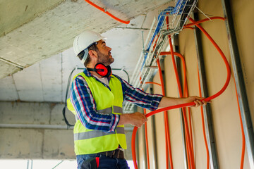 Wall Mural - An experienced electrician who stands on a ladder and adjusts cable bellows for the electrical network of the building where he works.