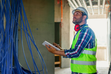 Wall Mural - An experienced electrical engineer who checks the cables in the building. He uses a tablet to help with work.