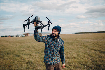 Man pilot holding quadcopter drone in hands at outside field