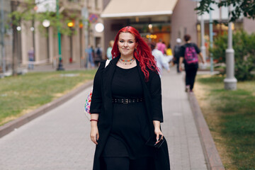 Wall Mural - European plus size woman walking outdoor street city. Young red pink haired body positive girl.