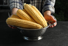 Woman With Colander Of Corn Cobs At Black Table, Closeup