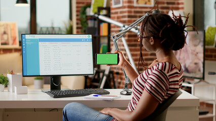 Poster - Young adult holding smartphone with horizontal greenscreen at home office desk. Looking at blank copyspace template with mockup background and isolated chroma key display. Tripod shot.