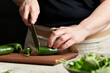 © The Picture Pantry - Hands slicing jalapenos on a cutting board.