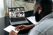 © Kateryna - Friendly african american man, sit at a desk in, having video meeting with colleagues, conducts financial brainstorm with business partners, takes notes. Group video meeting with multiracial people