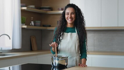 Wall Mural - Carefree happy young woman 30s housewife with curly hair wears apron dancing alone in kitchen cooking meal preparing food tasty dish soup porridge for children on electric stove active moving to music