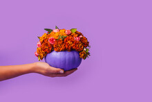 Happy Halloween Decorated Purple Pumpkin Decorated With Orange Flowers In Hand