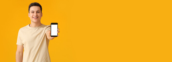 Wall Mural - handsome young man holding mobile phone on yellow background with space for text