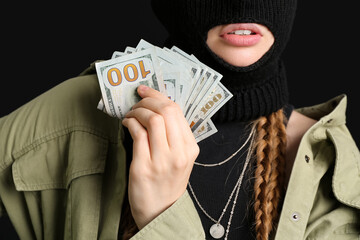 Wall Mural - Young woman in balaclava holding money on black background, closeup