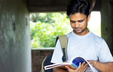 Wall Mural - Portrait of college student of indian origin using smartphone holding books in casual dress