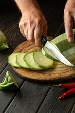 Hands Of A Chef With A Knife Cutting Vegetable Marrow On A Wooden Cutting Board Before Preparing Vegetarian Food.