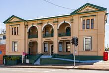 A Two Story Historic Building On A Sloping Corner Block With Traffic Lights In Front Of It
