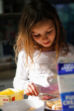 Blonde Girl Looking Down Holding A Butter Knife With Butter, Bread And Milk On For Breakfast