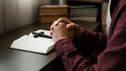 Hands together in prayer to God along with the bible In the Christian concept and religion, woman pray in the Bible on the wooden table.