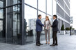 © Liubomir - Meeting of three colleagues from outside the office building, experienced and mature IT specialists, greeting and shaking hands, business persons in business suits, diverse group of people