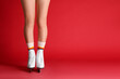 Woman in elegant white ice skates on red background, closeup of legs. Space for text