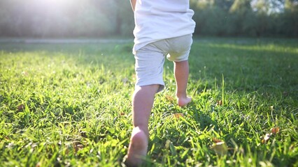 baby running in the park with bare feet. close-up of the kid leg runs in the summer on the green grass at sunset in the park. happy family kid concept. baby running and playing in the park dream