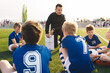 © matimix - Coach explains a game strategy using board. Young coach teaching kids on football field. Football coach coaching children. Soccer football training session for children. Football tactic education.