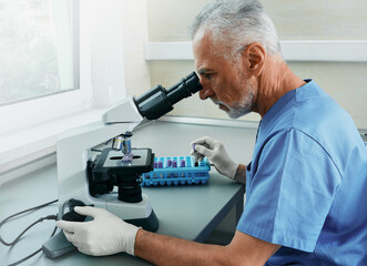 Professional male scientist looking in microscope while working on medical blood research in science medical lab