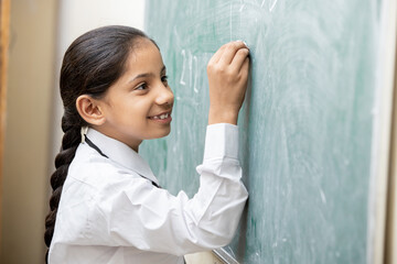 Happy Indian schoolgirl write on chalkboard or blackboard in classroom, Education concept.
