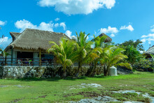 The Building With A Thatched Roof Is Surrounded By Palm Trees. Beautiful Landscape Of A Tropical Island. Bungalow In The Tropics.