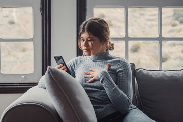 Portrait of impressed pretty female person staring phone bad fake news isolated on sofa at home. Young woman looking and reacting to something..