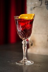 Poster - Vertical shot of a red cocktail in transparent goblet glass with and orange slice on the top