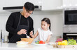 © atitaph - A happy family cooks together in the kitchen. The adorable father and little daughter prepare a salad for breakfast