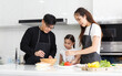© atitaph - A happy family cooks together in the kitchen. Father, mother, and cute little daughters prepare dishes for salads