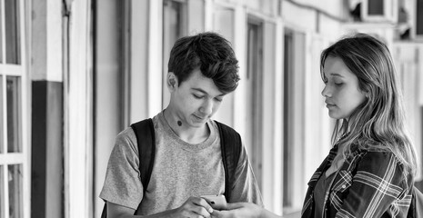 Wall Mural - Caucasian teenager couple slooking to the smartphone in the school hallway