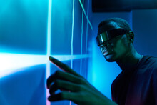 Young Black Man In Futuristic VR Goggles Touching Projector Screen